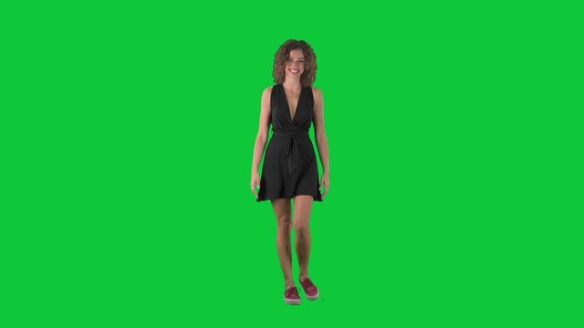 Pleased excited young woman walking and waving hand greeting on green screen chroma key background. 