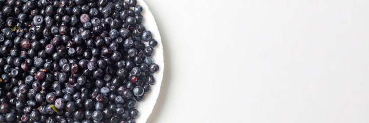 Blue delicious blueberries in a white plate on a white background top view