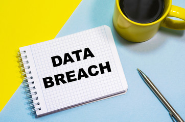 DATA BREACH on a notepad on a blue-yellow background, a cup of coffee and a pen. Business concept