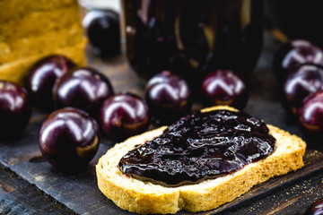 toast with grape jam, on rustic wooden table. Jabuticaba, exotic Brazilian fruit, used in cooking, as a sweet.