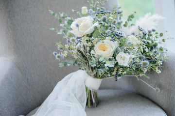 Bridal bouquet. The bride's bouquet. Beautiful bouquet of white, blue flowers and greenery, decorated with long silk ribbon lies on a gray textural background