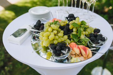 Table at the wedding ceremony with a buffet for guests: grapes, mulberries, apples, plates, napkins, glasses of champagne.
