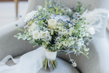 Bridal bouquet. The bride's bouquet. Beautiful bouquet of white, blue flowers and greenery, decorated with long silk ribbon lies on a gray textural background