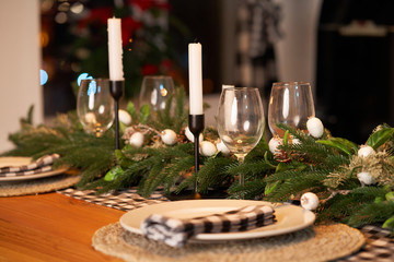 The festive Christmas table is decorated with branches of a Christmas tree, candles and garlands. Cozy home Christmas atmosphere.