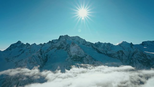 Snow capped mountains above clouds in a blue sky in sunny weather