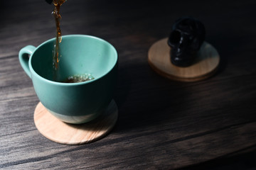 Cup of coffee on dark wood table and ornament in the background