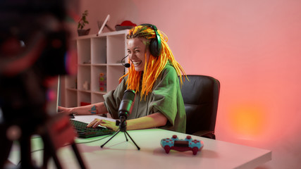 Adding Fun. Female esport gamer, woman in headphones looking focused, playing online video game on PC while recording, filming vlog at home © Svitlana