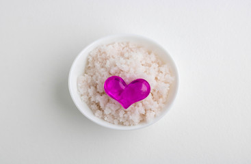 An oval white bowl with pink salt and a pink heart stands on a white background