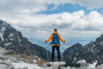 Dressed bright orange jacket backpacker man with trekking poles enjoying the mountain valley view...
