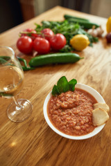 Close up of bowl of tomato soup or Pappa al Pomodoro served with a glass of white wine. The soup with tomatoes and bread, traditional Italian Tuscan dish