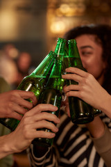 Good vibe for good night. Close up of hands of people in the bar clinking bottles while drinking beer together. People, leisure, friendship and entertainment concept