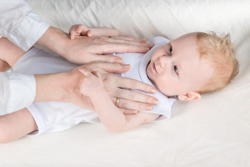 Obraz na płótnie Canvas Womens hands massage a beautiful baby in a white bodysuit. Stroke. The baby is lying on the changing table