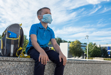 Boy, schoolboy in protective mask sits near the school in sunny September day