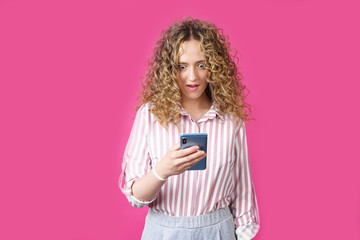 A fashionable woman in a striped shirt, holds a mobile phone, gasps in surprise, reads amazing news.