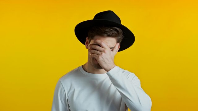 Frustrated european man in white wear and hat over yellow wall background. Guy is tired, bored of work or studying, he disappointed, helpless