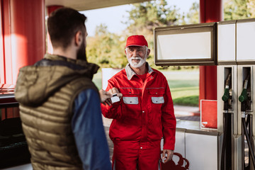 Young handsome adult man together with senior worker standing on gas station and fueling car.