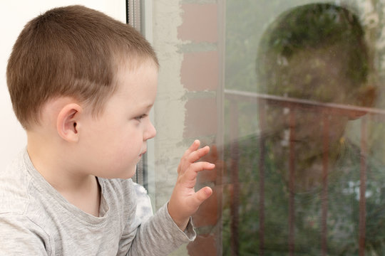 A Little Sick Boy Looks Out The Window. Insulation Of The House. Stay At Home In Quarantine For The Coronavirus.