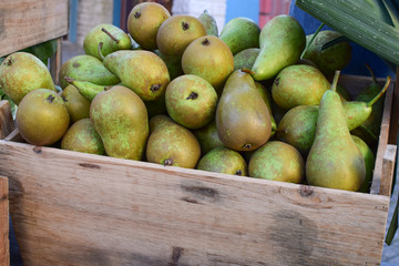 Green pears in a wooden box on the market counter.