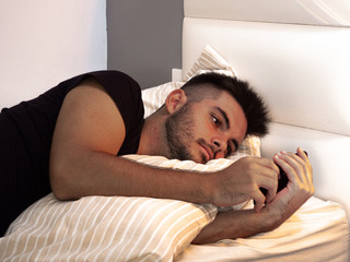 Adolescente usando el teléfono móvil en la cama abrazando la almohada con una camiseta negra...