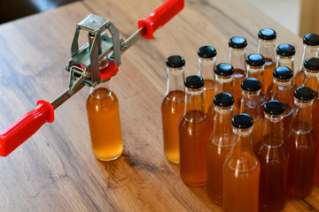 Naklejka premium Using hand capper for home brewing. Background of brown bottles with homemade liquor or alcohol. Selective focus.