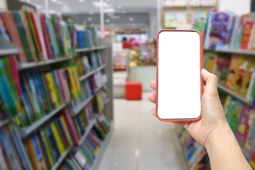 Hand of a man holding smartphone device in the Bookstore background.