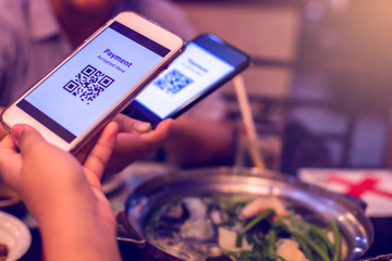 Selective focus to smartphone in hand to scan QR code tag 
with blurry Chinese food (Suki) and dessert in restaurant to accepted generate digital pay without money. Qr code payment concept.