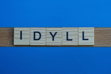 gray word idyll in small square wooden letters with black font on a blue background