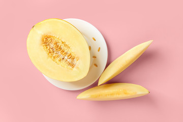 Half of yellow ripe honeydew melon on white plate and two slices over pastel pink background. Vegetarian, raw food diet and healthy eating concept. Sweet fruits and berries.