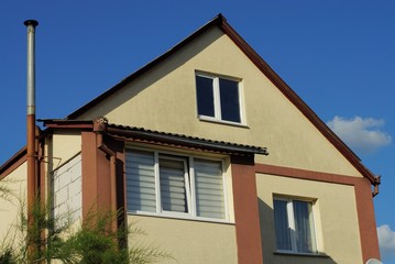 facade of a brown private house with white windows against a blue sky