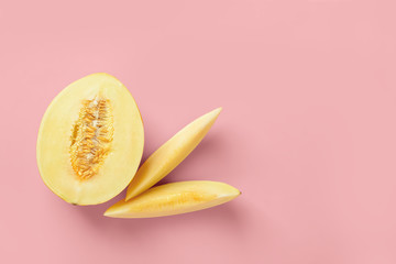 Half and two slices of yellow ripe honeydew melon over pastel pink background. Vegetarian, raw food diet and healthy eating concept. Sweet fruits and berries. Copy space.