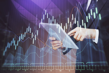 Double exposure of man's hands holding and using a digital device and forex graph drawing. Financial market concept.