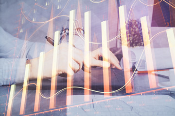 Double exposure of man's hands holding and using a phone and financial graph drawing. Analysis concept.