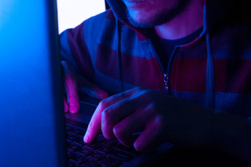 hacker or programmer typing on a keyboard in a room in the dark, young man hacking computer