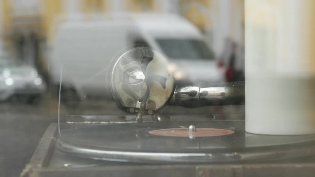 Vintage gramophone with old-fashioned vinyl record disc in a shop window display of a cafe with reflection of the street and passing cars. Old mechanical turntable music player with metal needle head