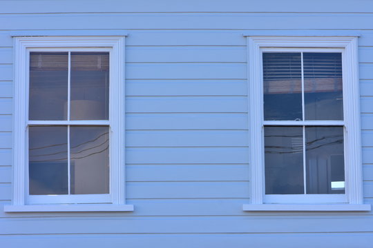 Vintage windows with four glass panes on wooden pale blue wall with weatherboard cladding.