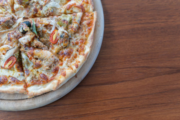 Homemade pizza with tomatoes, olives, salami, mozzarella cheese and seafoog on wooden rustic table.