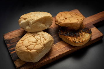 
homemade whole and sliced ​​burger potato bread toasted on wooden board on black background