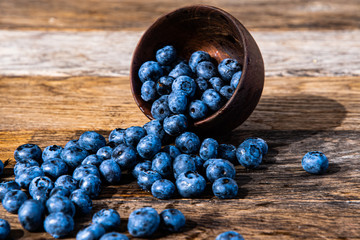 Black rowan fruits overturned in a wooden dish on a rustic wooden table.
