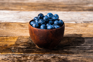 Black rowan berries in a wooden bowl on a rustic wooden table.