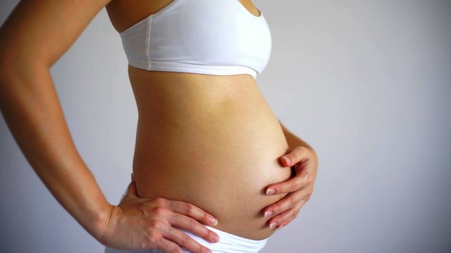 The profile of the body of a young pregant woman on a white background