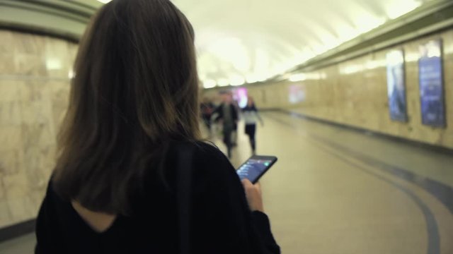 Rear view of a young woman wearing black sweater walking out of metro station. Media. Girl walking slowly through the long corridor of subway station.