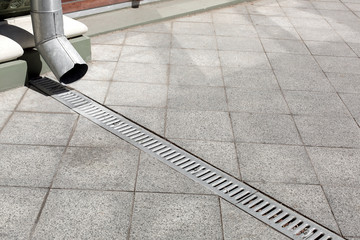 galvanized downspout on facade building with iron drainage grate of gray stone granite sidewalk from square tiles on ground, closeup details city infrastructure, nobody.