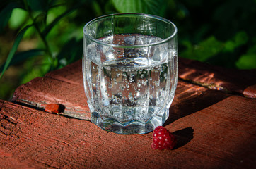 A glass with mineral, carbonated water raspberry berry, on a wooden board in the garden.