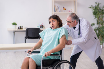Young male patient in wheel-chair and experienced doctor traumatologist