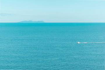 Blue clear sky and turquoise sea landscape. A boat floats in the distance. Summer sea bay. Vladivostok, Russian island, Chernyshev bay.