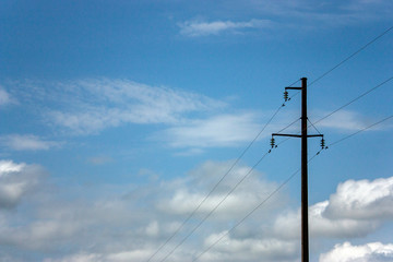 High-voltage line of electrical wires in a field against a blue sky with white clouds. Lonely pillar with wires across the sky.