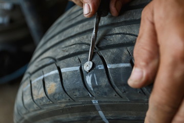 solve problem wheel in garage auto repair shop service. replacement repairman fixing car's tire trying to remove nail from hole. Flat tire. Accident with punctured tires concept.