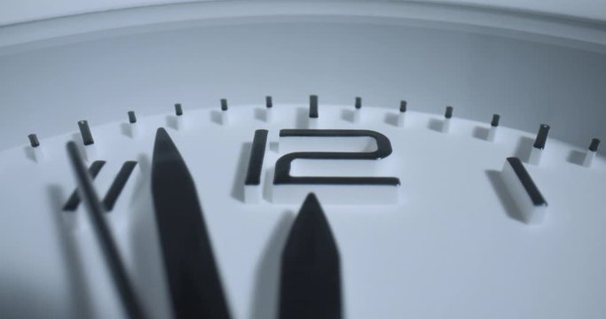 Seconds Pass High Noon. Extreme macro wide angle close up as the second hand ticks past the 12 (noon/midnight) on a small alarm clock with raised 3D numbers.
