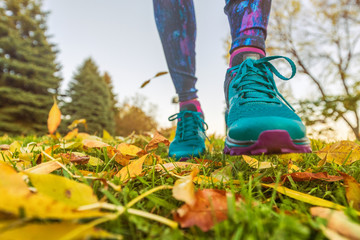 Walking outdoor in autumn nature park. Woman going outside taking a step with running shoes in yellow fall leaves.