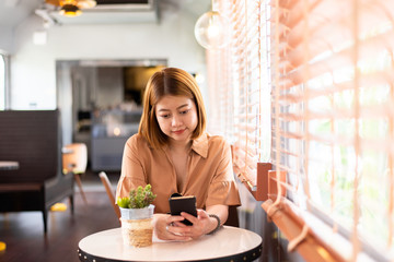 Happy young asian woman using mobile phone while sitting in cafe